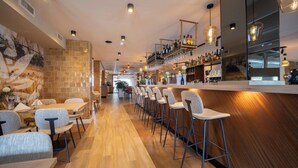 A modern bar area with wooden flooring, bar stools, and a long counter with shelves of bottles.
