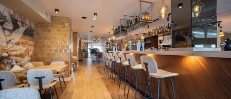 Un área de bar moderna con suelo de madera, taburetes y una barra larga con estantes llenos de botellas.