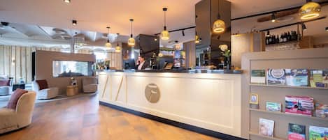 A modern hotel lobby with a wooden floor, a reception desk, and a seating area with sofas.
