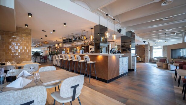 A spacious restaurant with a long counter, multiple bar stools, and a bar area with shelves of bottles.