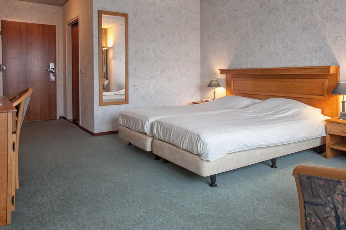 Habitación de hotel con una cama doble, una mesita de noche de madera con lámpara, un escritorio y una silla.