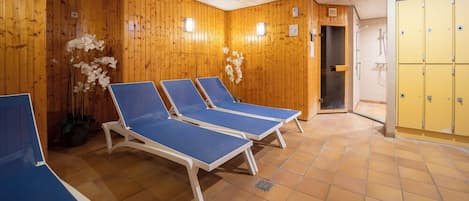 Um quarto com paredes de madeira, poltronas de descanso azuis e armários amarelos.