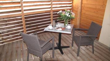 Une terrasse en bois avec deux fauteuils en osier et une table, une bouilloire en métal et un vase rempli de fleurs.
