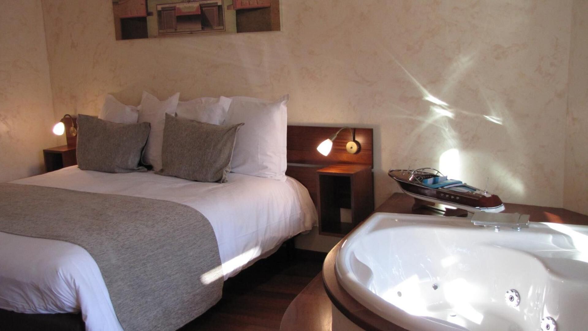 A bedroom with a bed, pillows, bedside tables, a lamp, and a bathtub.