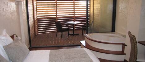 A bedroom with a large bed, a small table, a chair, and a bathtub.