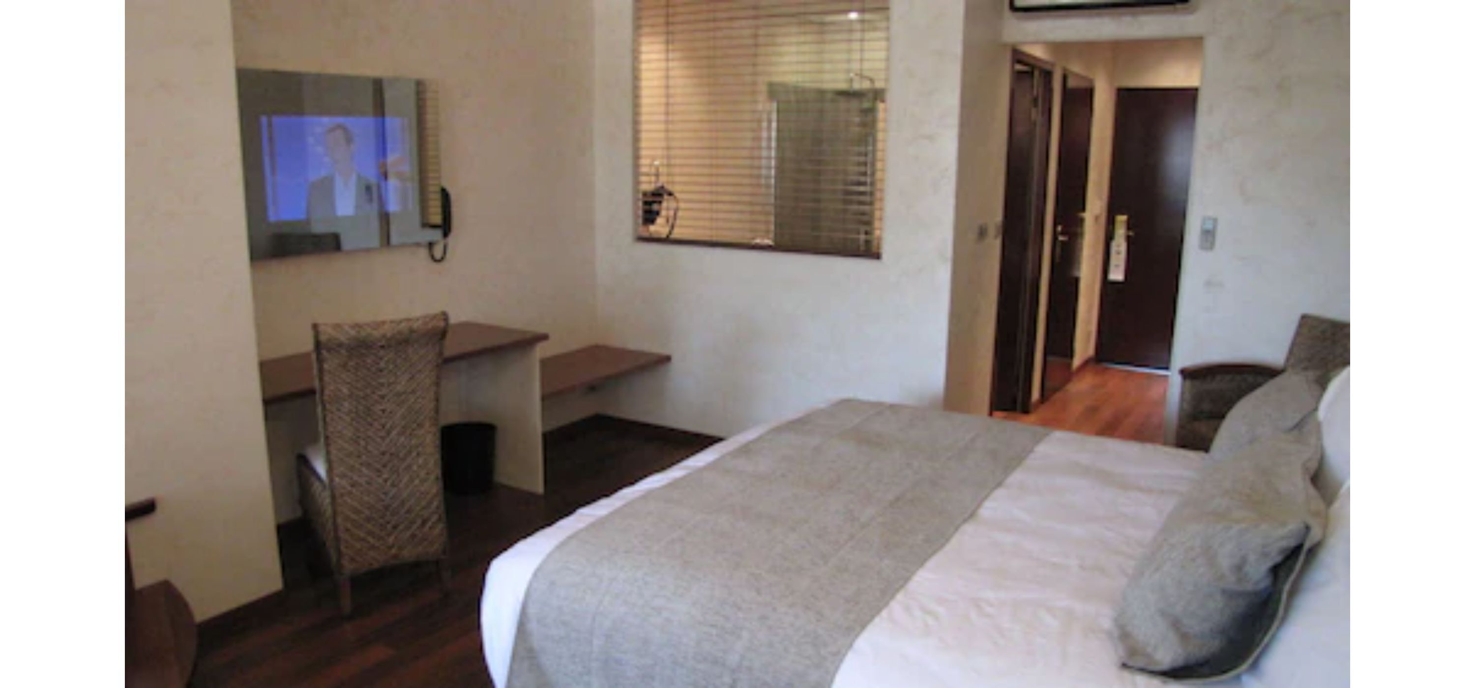 Une chambre d’hôtel comprenant un lit, un bureau avec une chaise, une télévision et une fenêtre avec des stores.