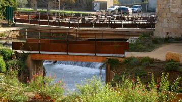 A bridge with seating overlooking a flowing river, surrounded by greenery and a stone wall.