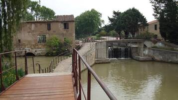 A wooden bridge over a calm river with a stone building on the left and a bridge on the right.
