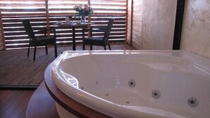 Una habitación con una tina de hidromasaje grande y redonda, piso de madera, una mesa con sillas y un jarrón con flores.