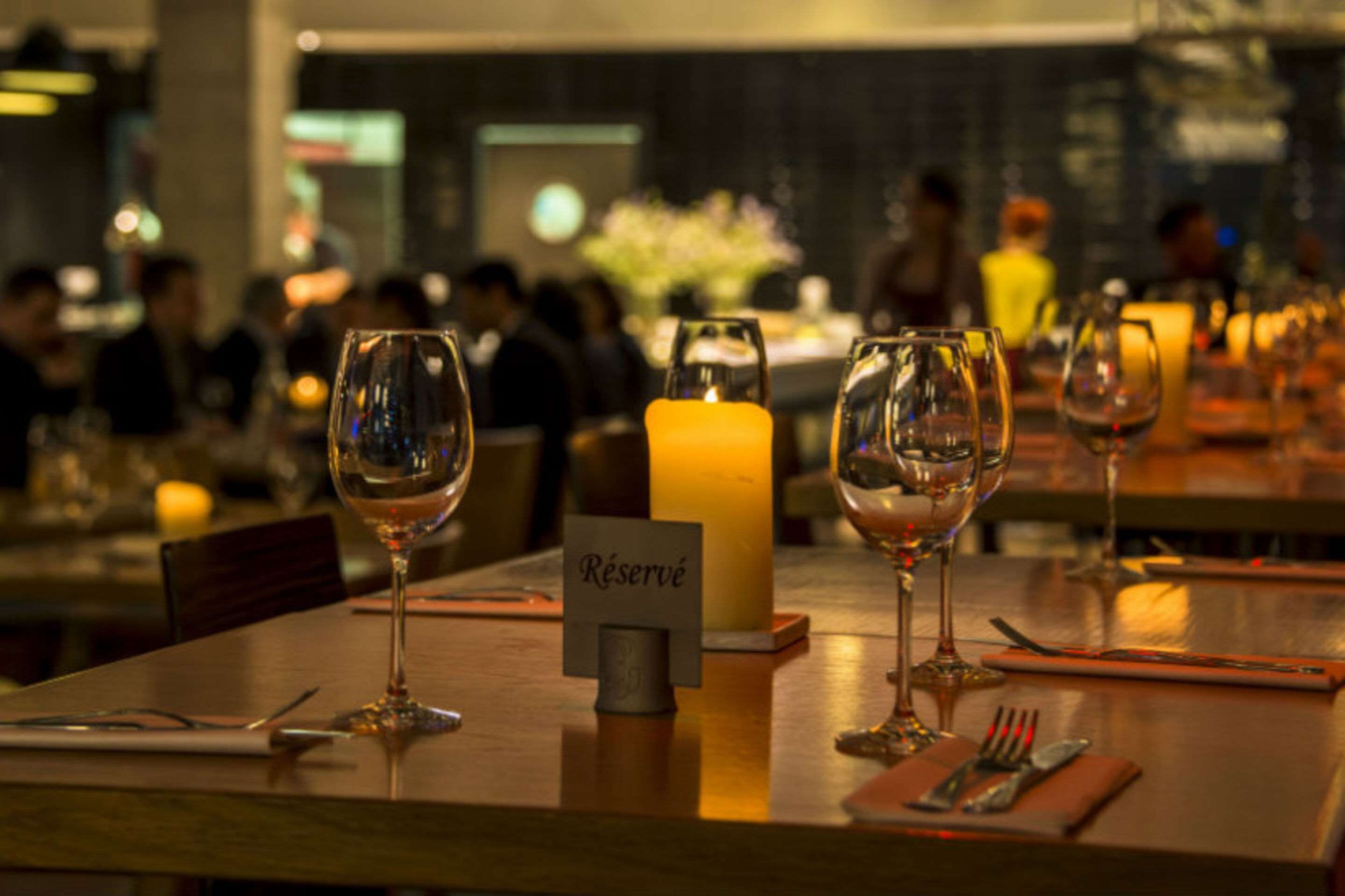 A restaurant setting with tables set for dining, a candle centerpiece, and a 'Réservé' sign indicating a reserved table.