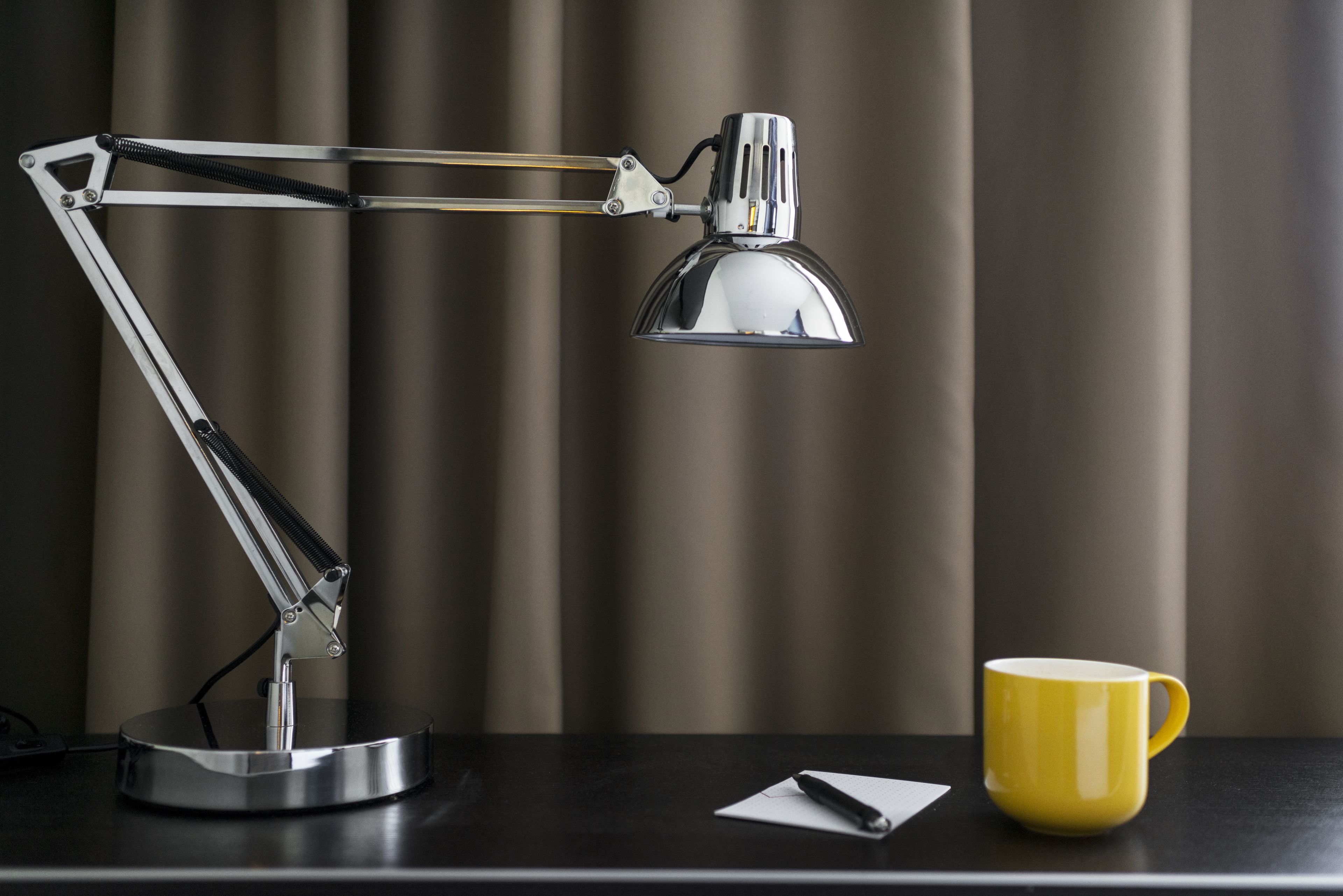 Un bureau avec une lampe de bureau métallique et une tasse jaune.