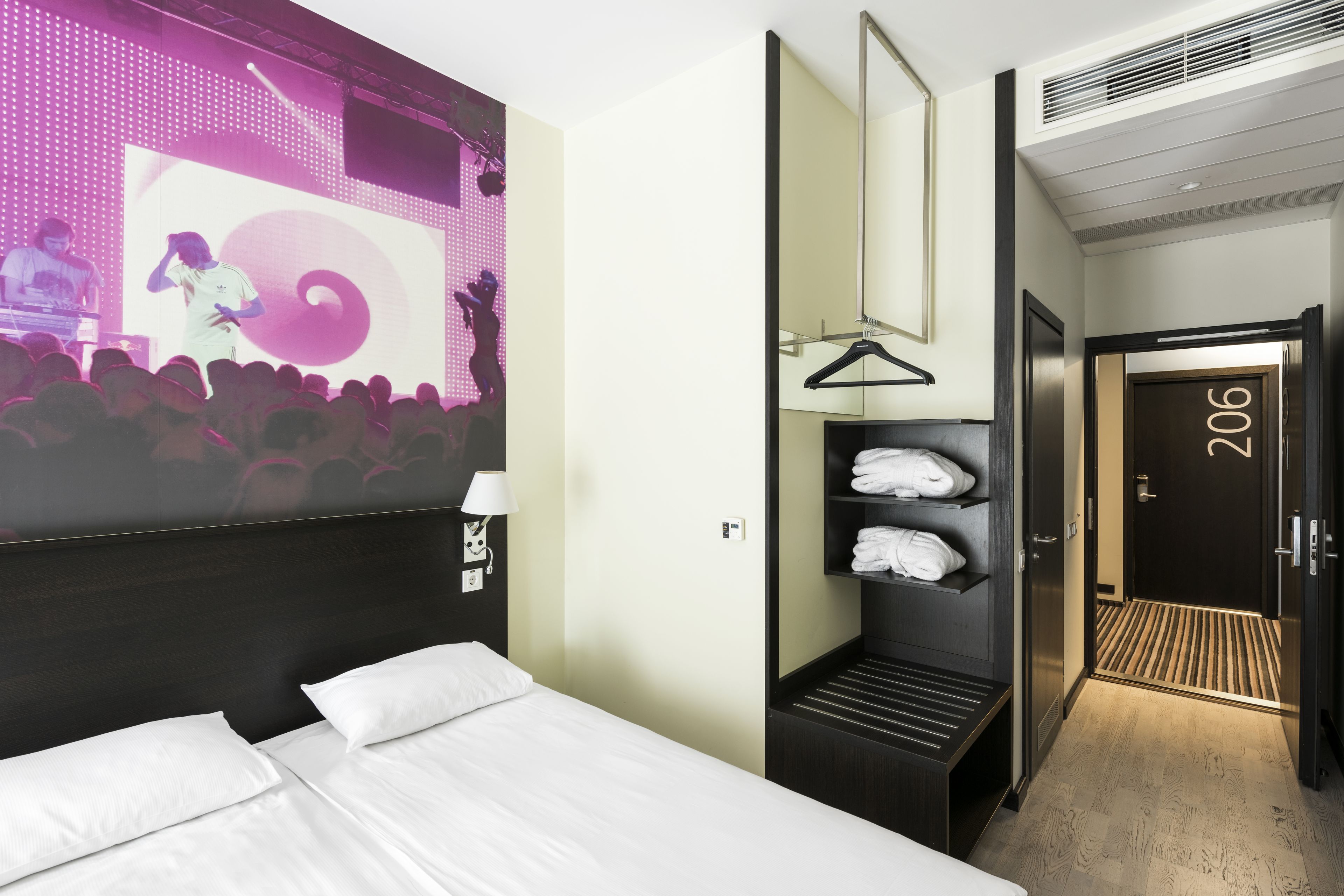 Une chambre d’hôtel avec un lit, un miroir, un porte-serviettes et une porte portant le numéro 206.