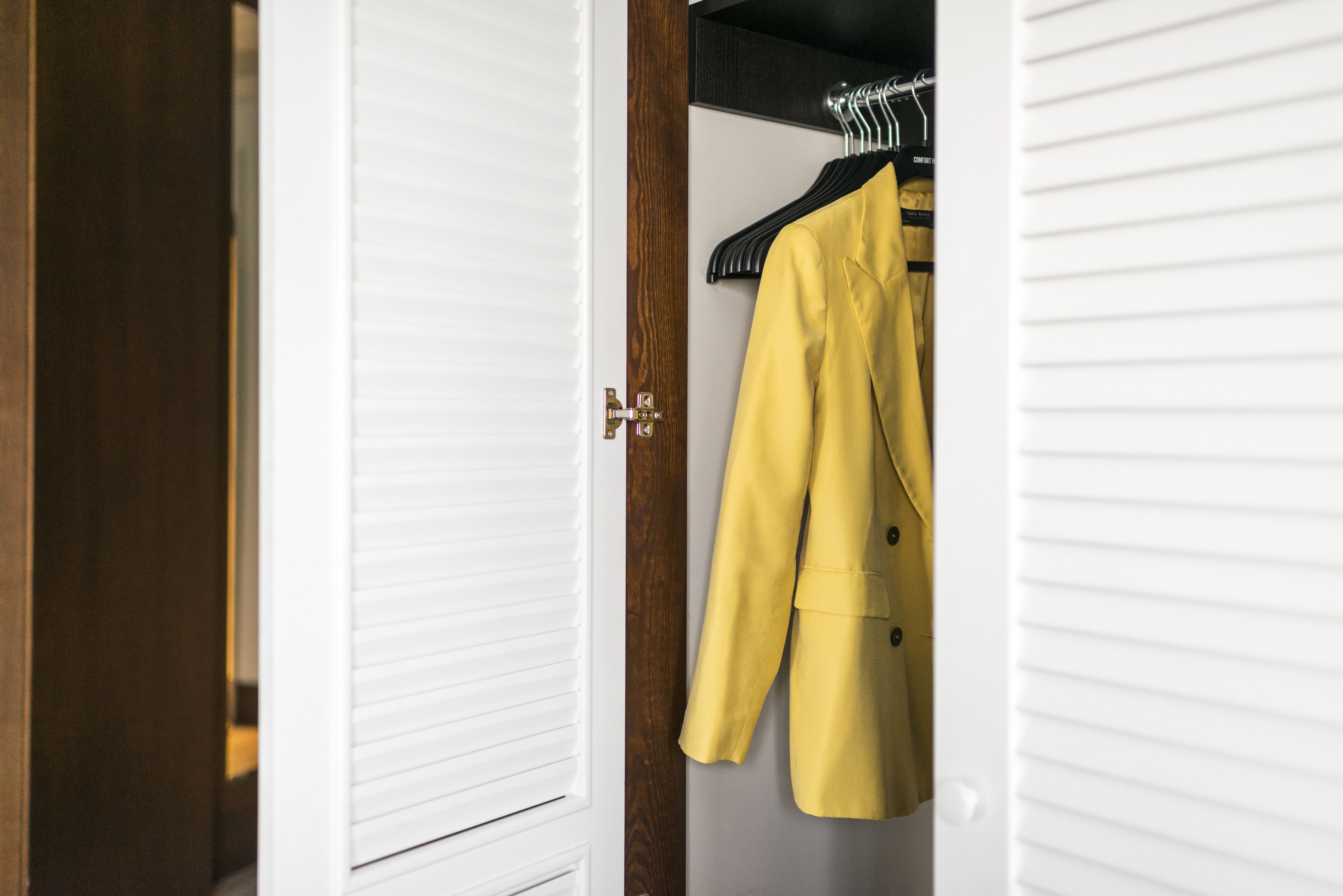 A wardrobe with a yellow coat hanging on a black hanger.