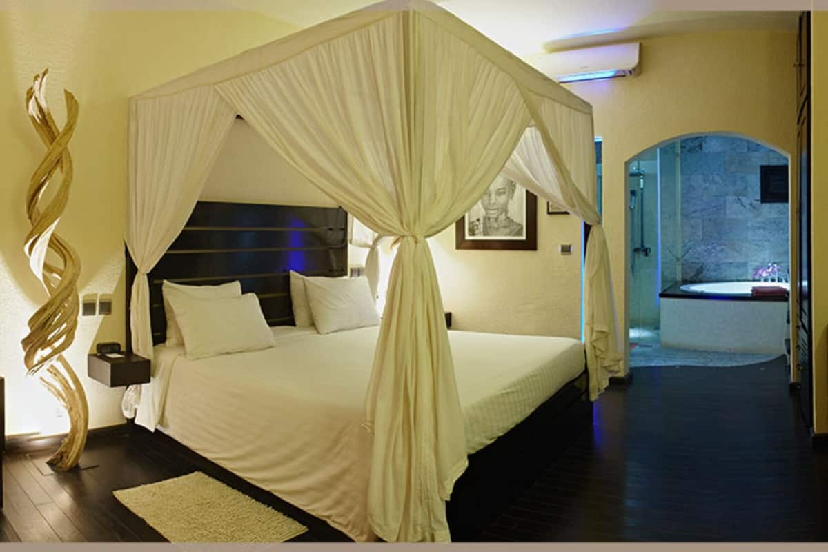 Quarto com cama de dossel, mesa de cabeceira, cadeira e cômoda.