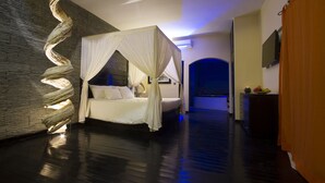 A modern bedroom with a canopy bed, a stone accent wall, and a flat-screen TV on a dresser. - The Rhino Resort Hotel & Spa (Mbour)