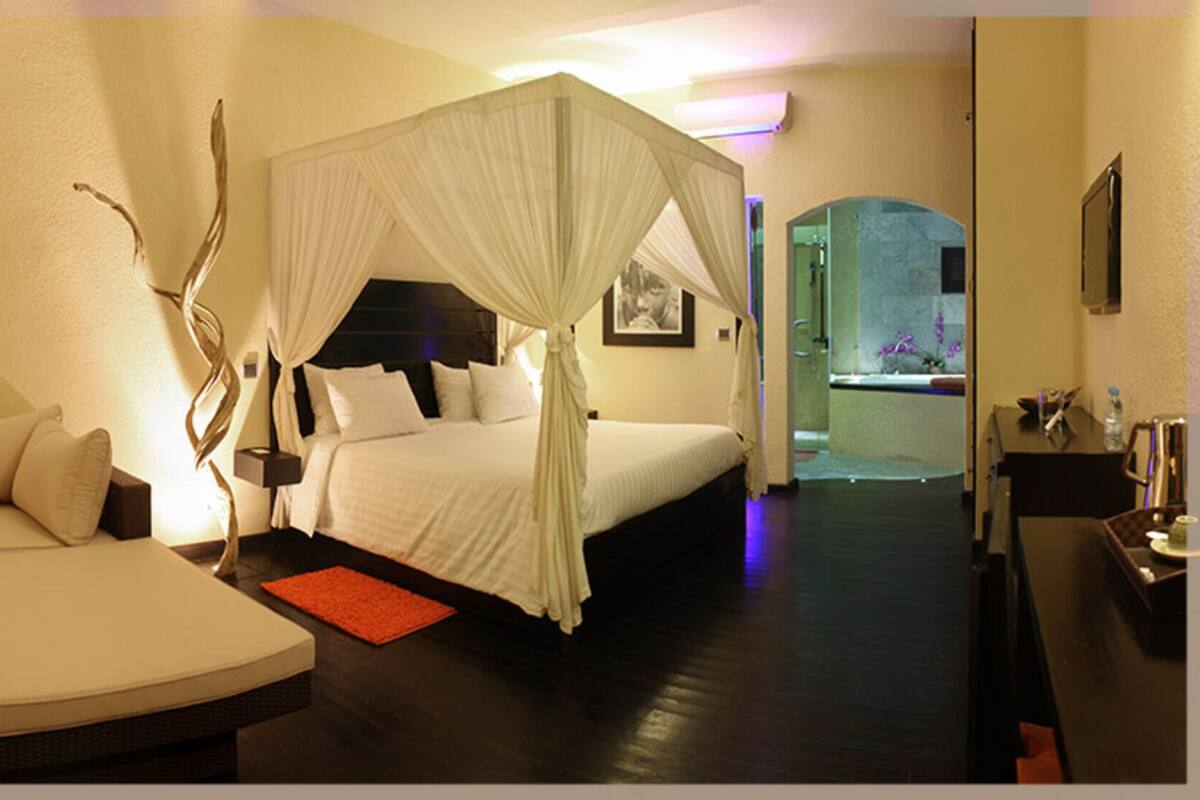 Quarto com cama, sofá, mesa de cabeceira, abajur e um quadro na parede.