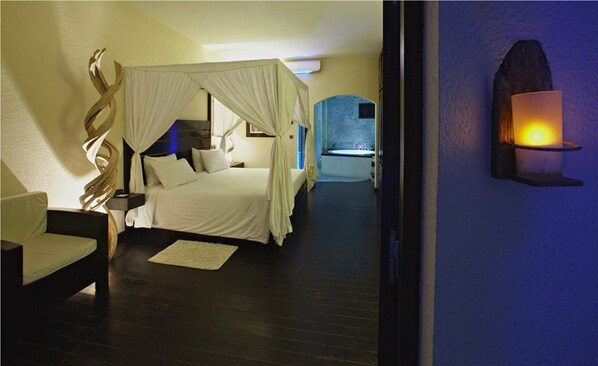 Un dormitorio con cama con dosel, una zona de estar con una butaca y un aplique de pared.