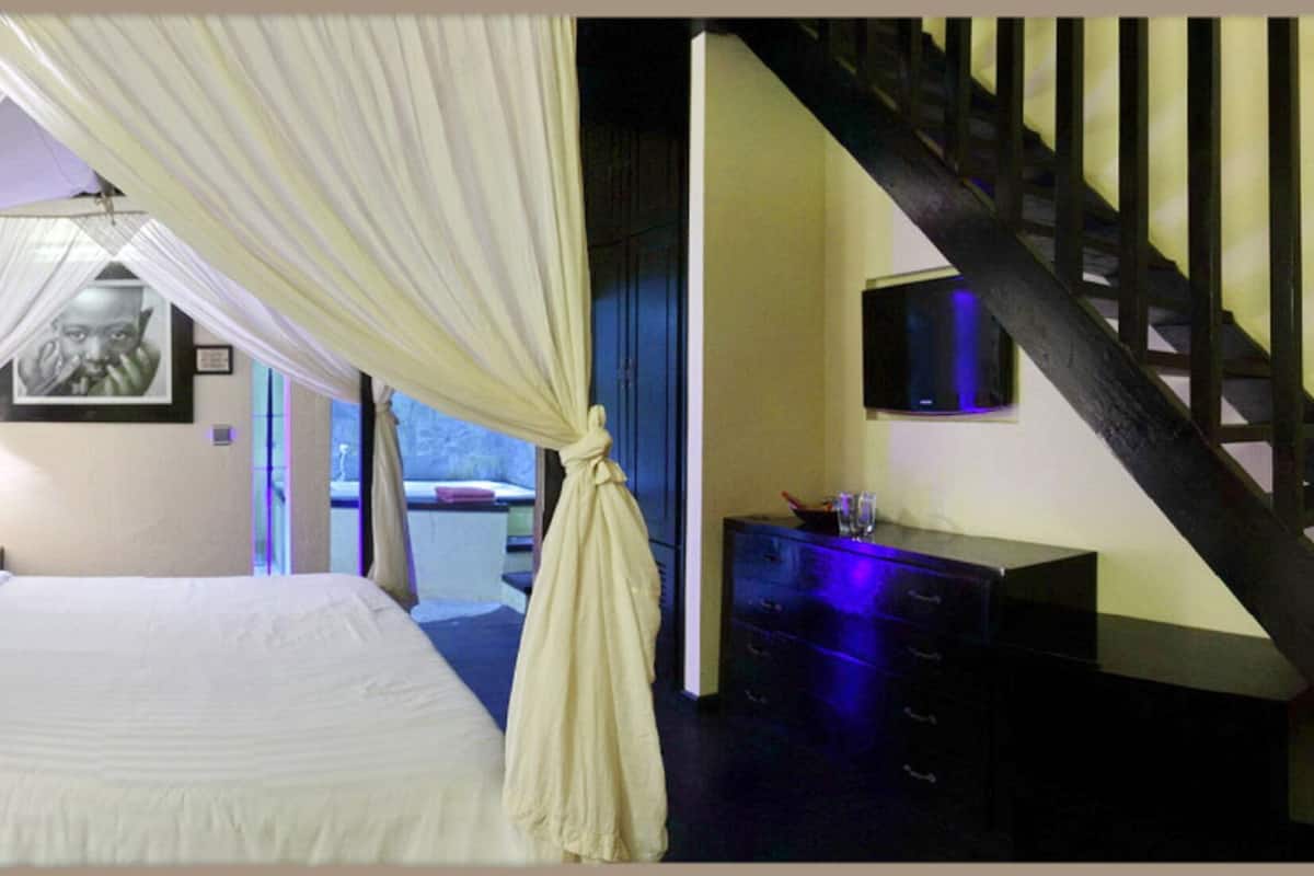 Quarto com cama, mesa de cabeceira, cômoda, televisão e escada.