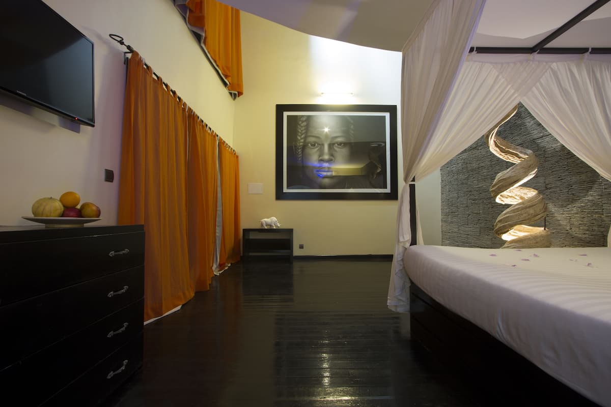 Quarto com cama, cómoda, televisão e uma obra de arte emoldurada na parede.
