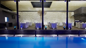 A poolside area with tables and chairs, a stone wall, and a modern ceiling design. - The Rhino Resort Hotel & Spa (Mbour)