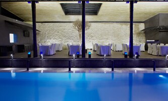 Zona junto a la piscina con mesas y sillas, pared de piedra y diseño moderno de techo.