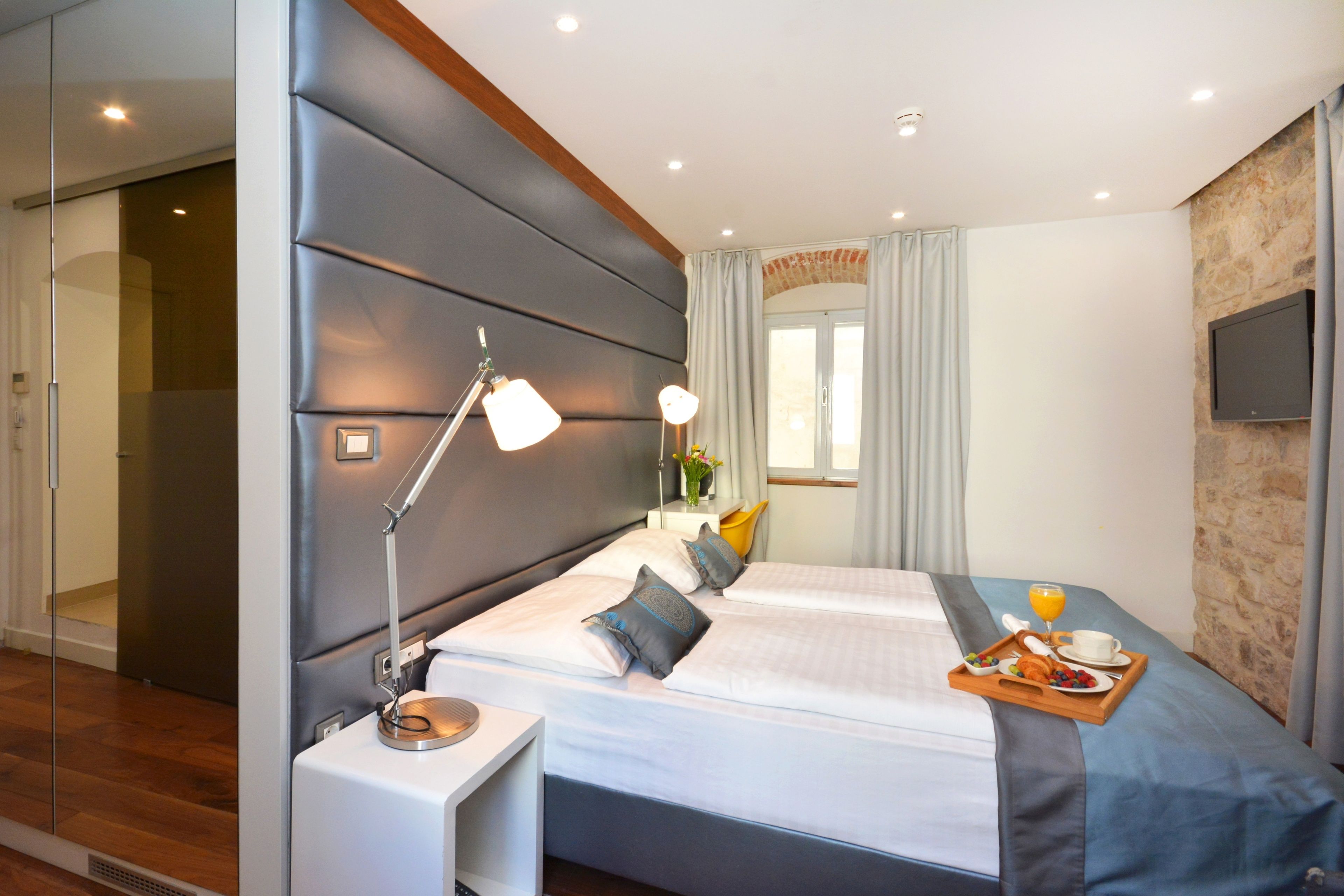 A modern hotel room with a large bed, bedside tables, a TV, and a breakfast tray on the bed.