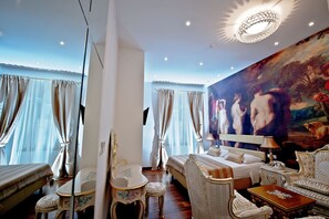 A room with a bed, a sofa, a chair, a table, and a large painting on the wall. - Heritage Jupiter Luxury Hotel (Split)