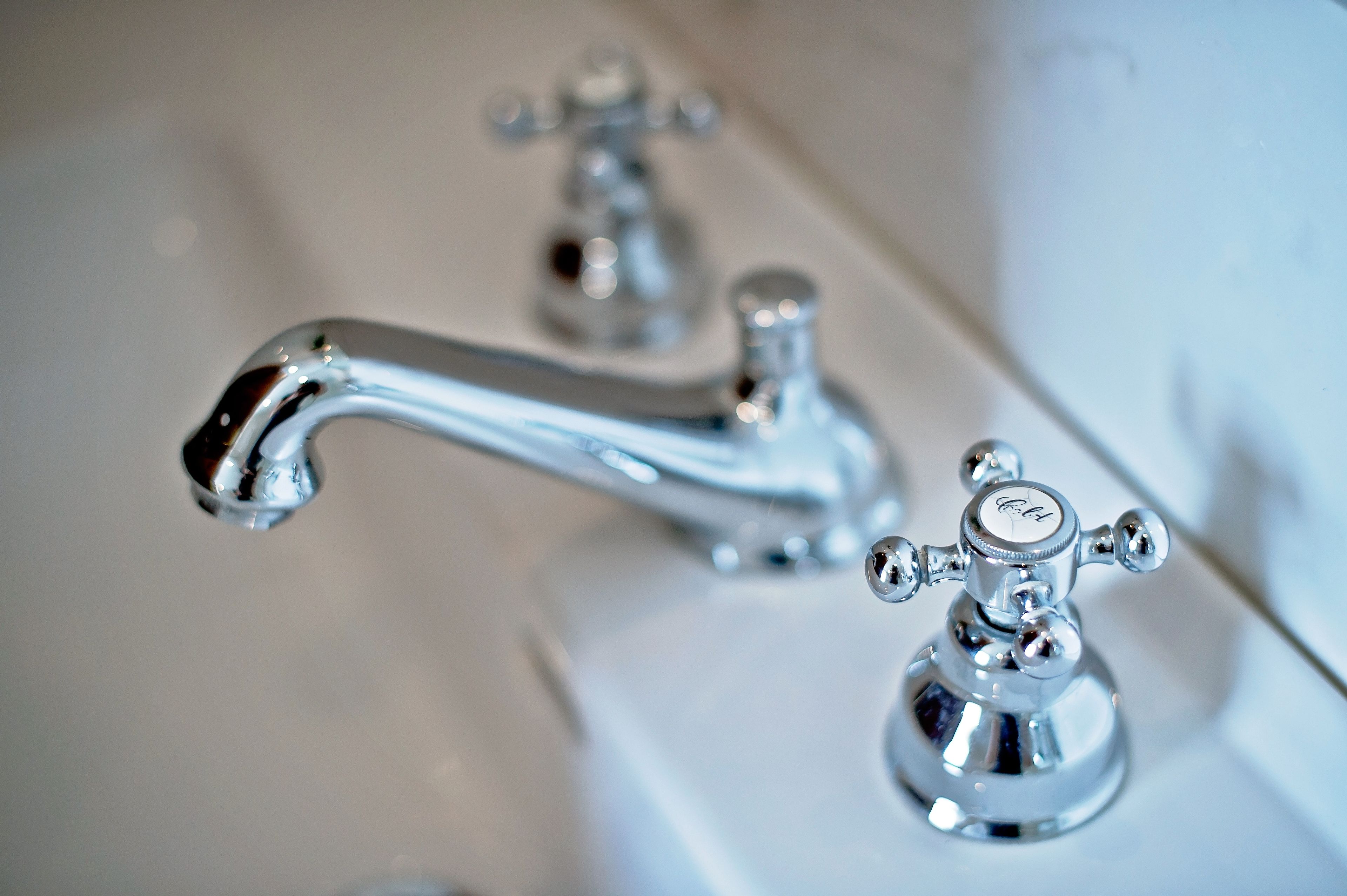 Ein Detailaufnahme eines chromfarbenen Wasserhahns mit einem Hebel und einem separaten Drehknopf, beide auf einem weißen Waschbecken montiert.