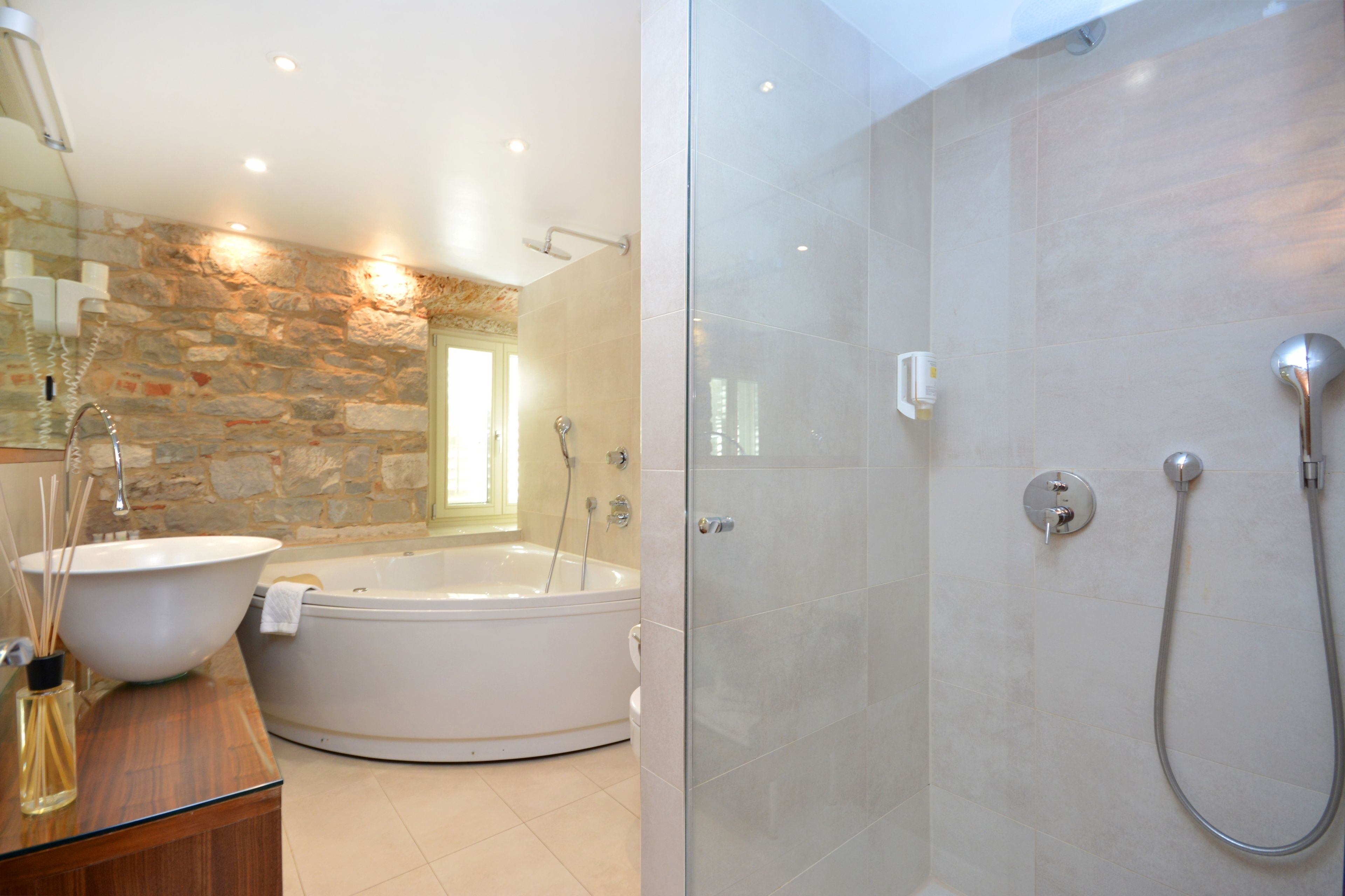 A modern bathroom with a stone wall, a large bathtub, and a walk-in shower.