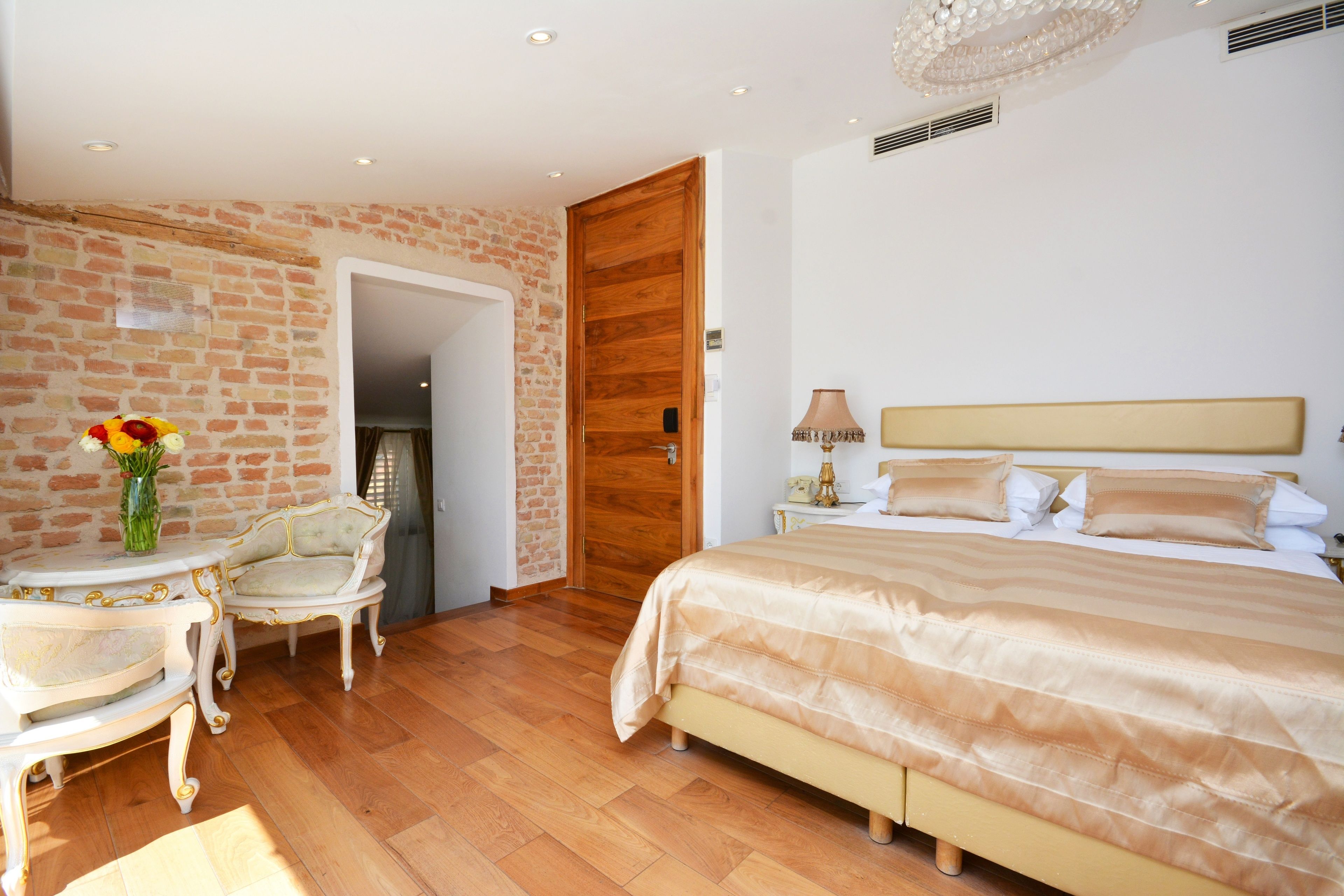 Une chambre à coucher avec un lit, une table de chevet, une lampe, une chaise et un vase de fleurs.