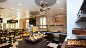 A buffet area with a variety of food options, including fruits, vegetables, and bread. There are multiple dining tables and chairs arranged in the space. - Heritage Jupiter Luxury Hotel (Split)