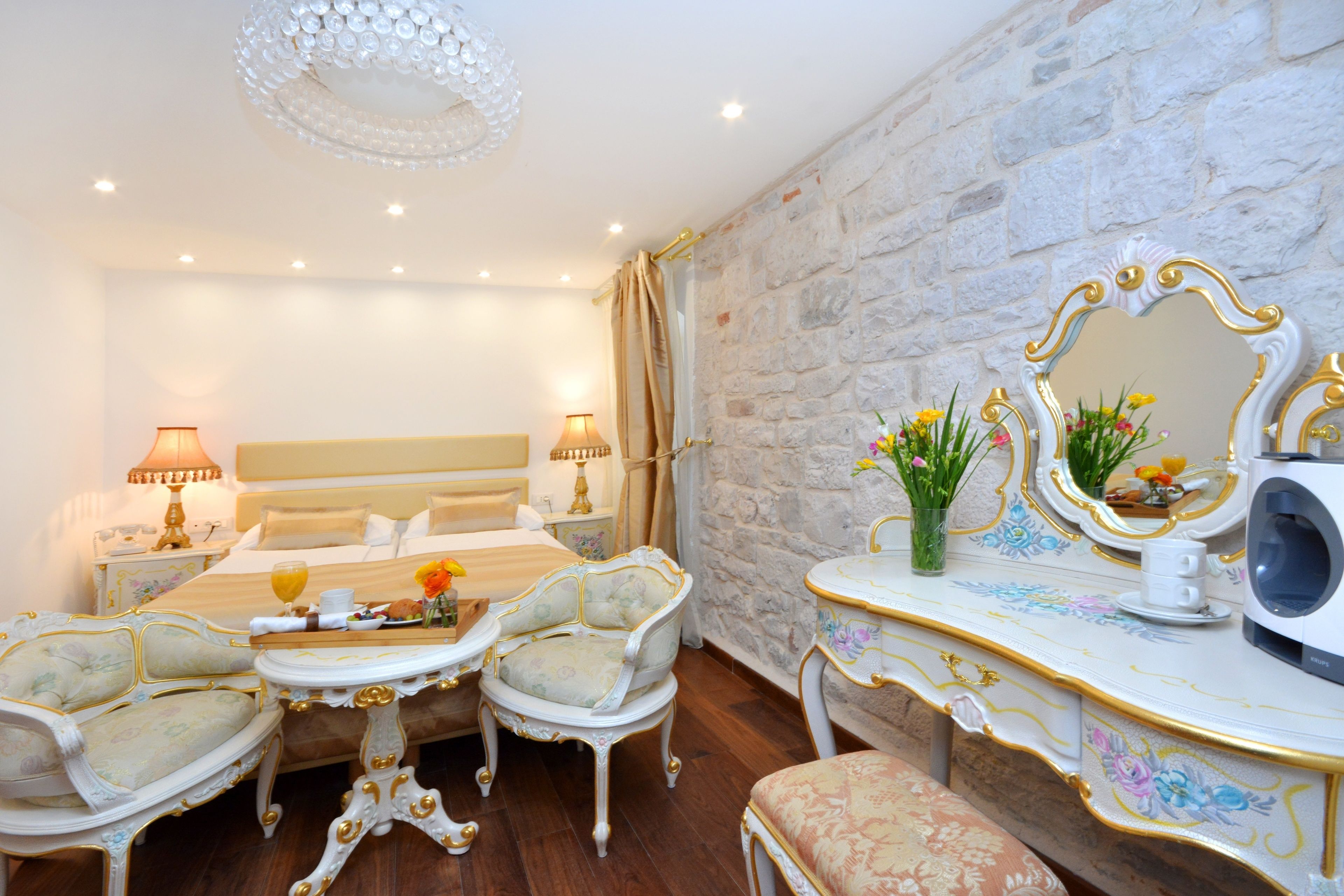 A luxurious bedroom with a stone wall, a large bed, ornate furniture, and a decorative mirror.