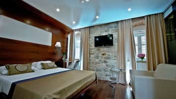 A hotel room with a bed, a TV mounted on a stone wall, a chair, and a window with curtains.