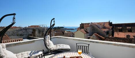 A rooftop terrace with a table set for breakfast, a lounge chair, and a clear view of the cityscape.