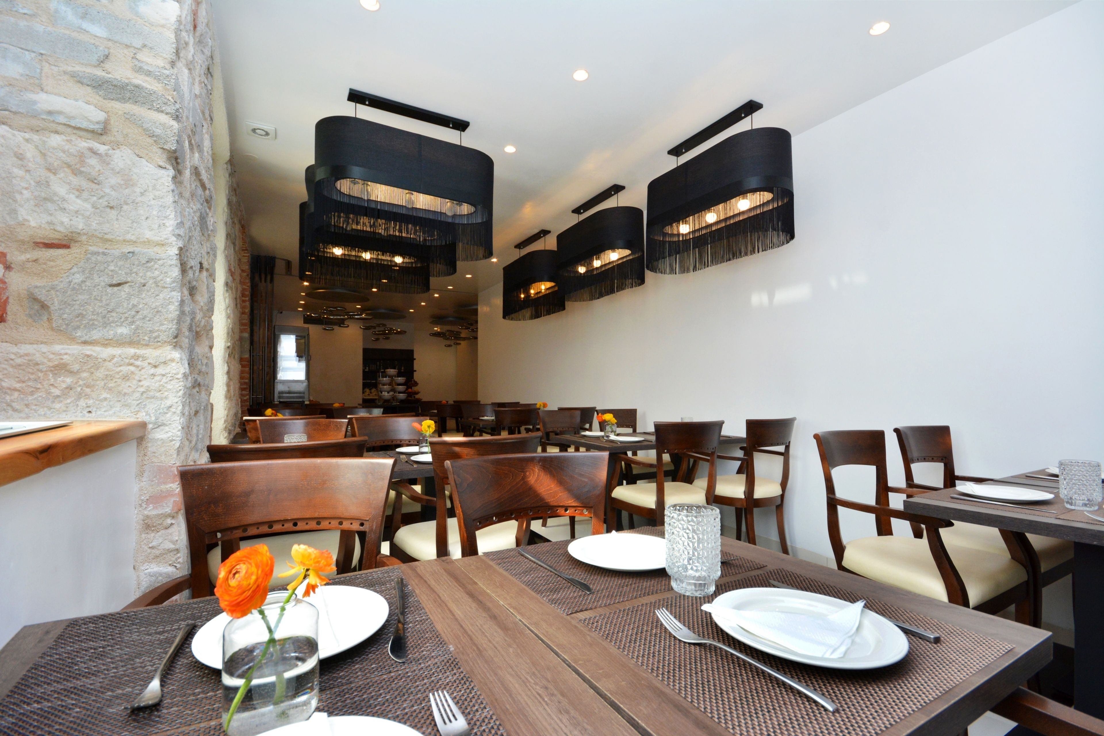 Un restaurant avec des tables et des chaises en bois, un mur en pierre et des lampes suspendues.