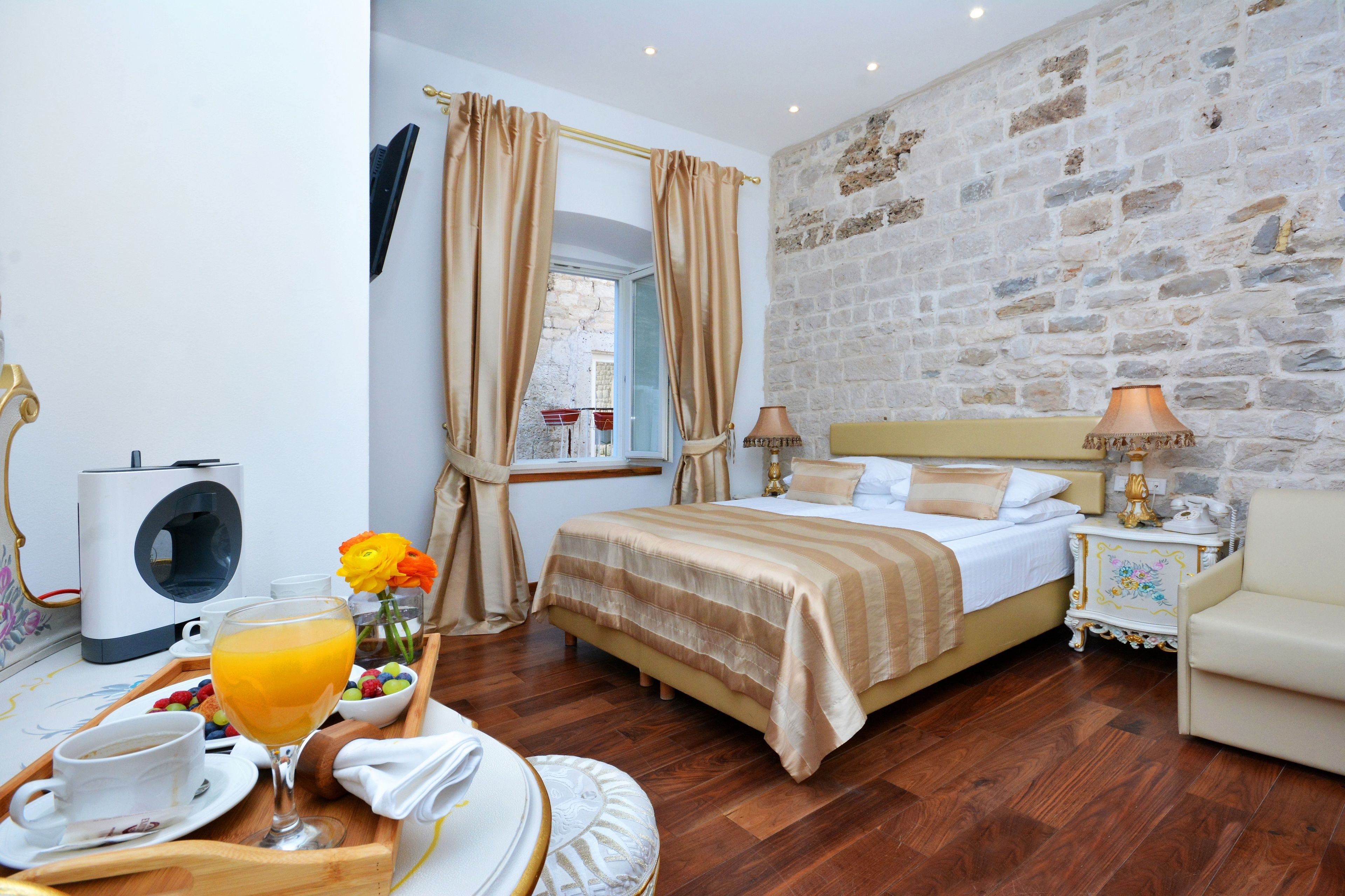 A hotel room with a bed, bedside table, lamp, and a breakfast tray with orange juice and pastries.