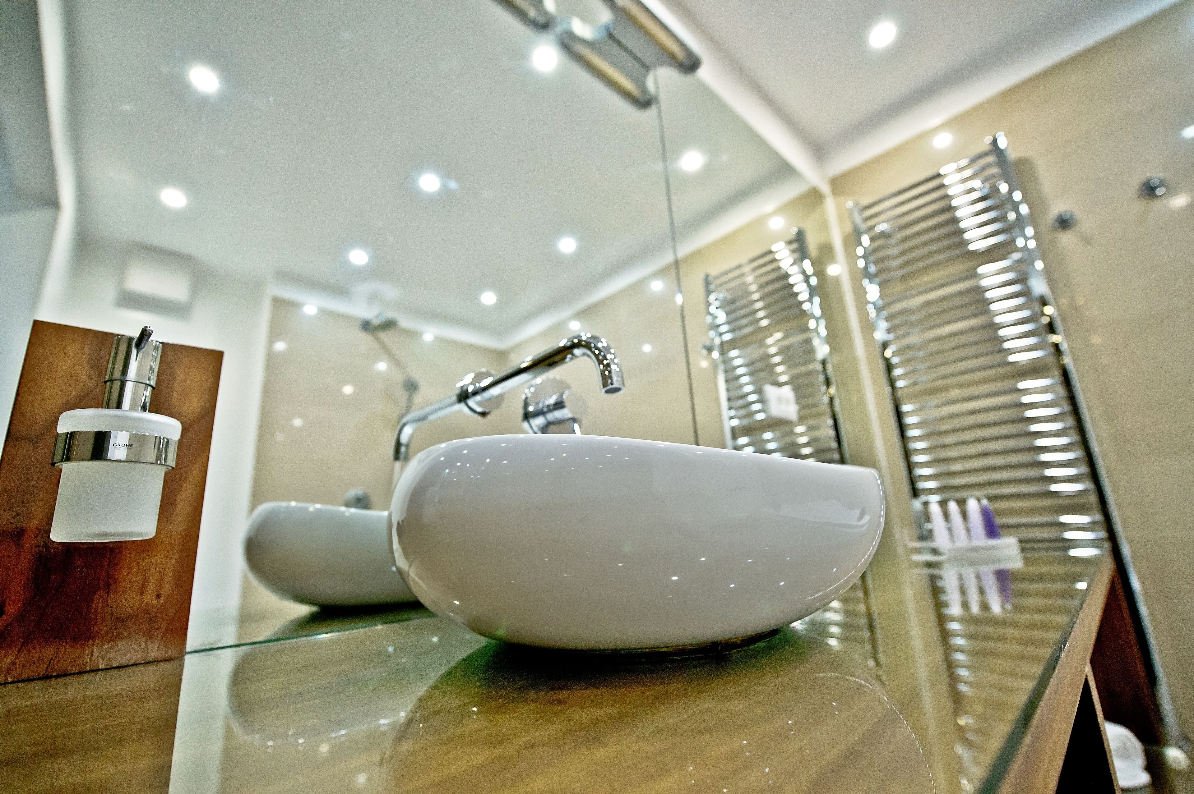 A modern bathroom with a white sink, chrome faucet, and a glass countertop.
