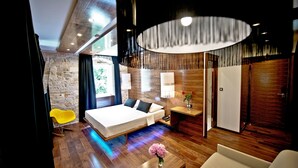 A modern hotel room with a large bed, a wooden floor, a small desk with a lamp, and a view of the outdoors. - Heritage Jupiter Luxury Hotel (Split)