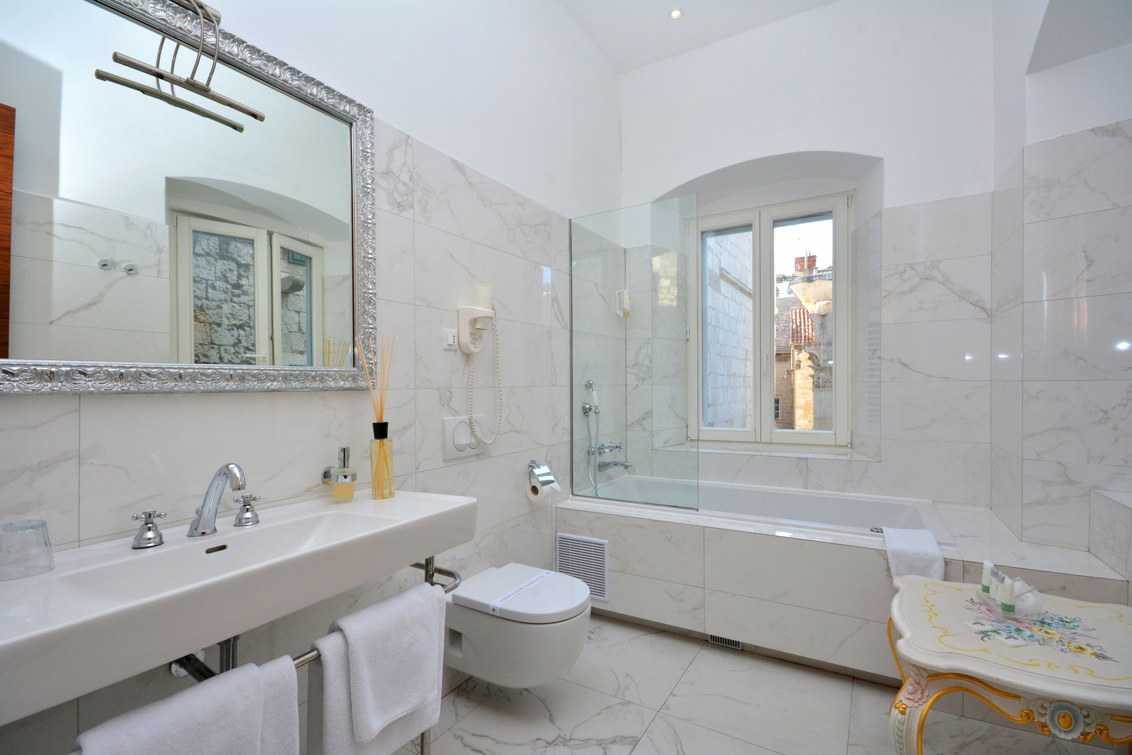 A modern bathroom with a large mirror, a bathtub, a toilet, and a vanity with a sink.