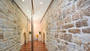 A hallway with stone walls and wooden flooring, leading to a room with a yellow chair and a plant. - Heritage Jupiter Luxury Hotel (Split)