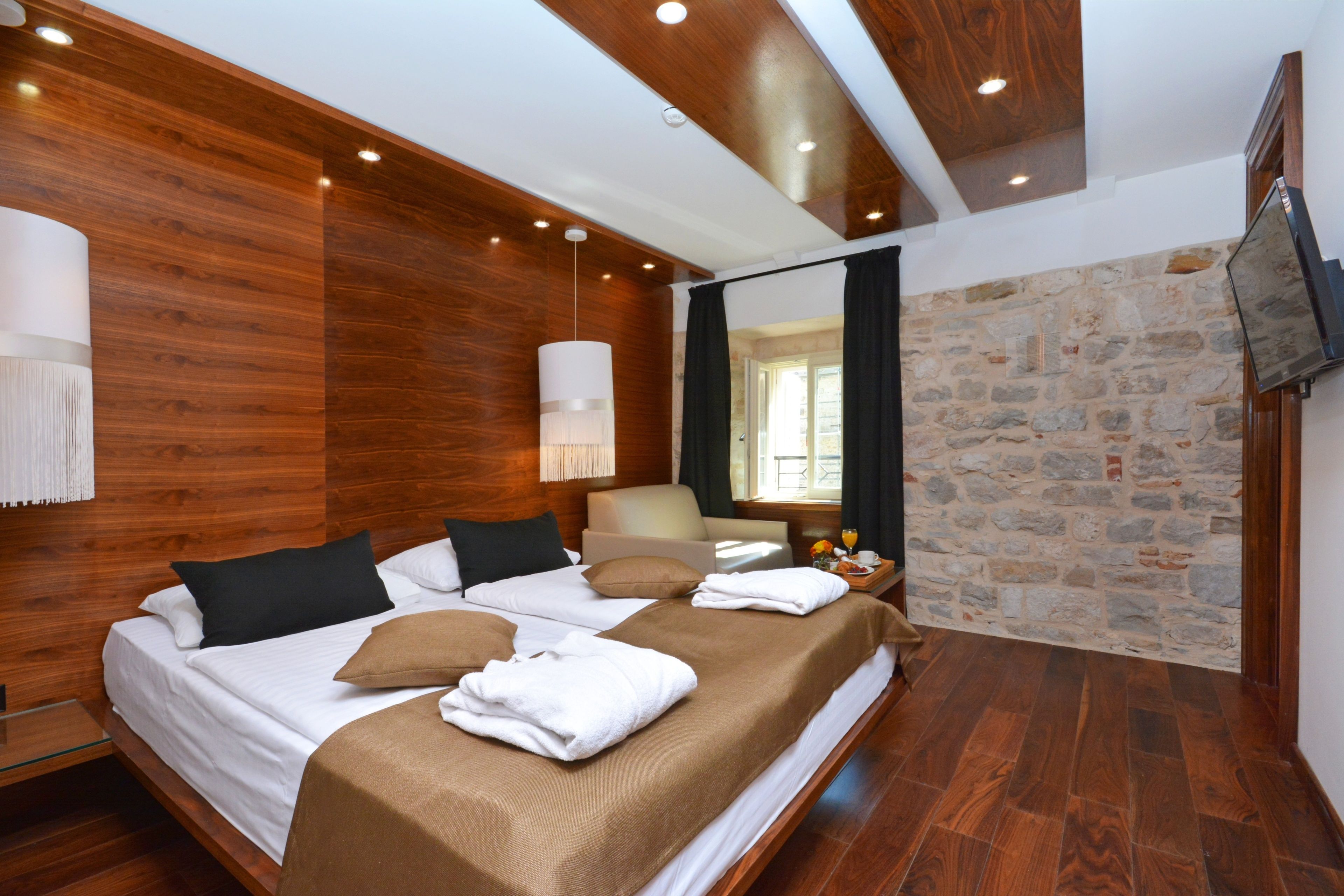 A modern hotel room with a wooden ceiling, a stone wall, and a large bed with towels.