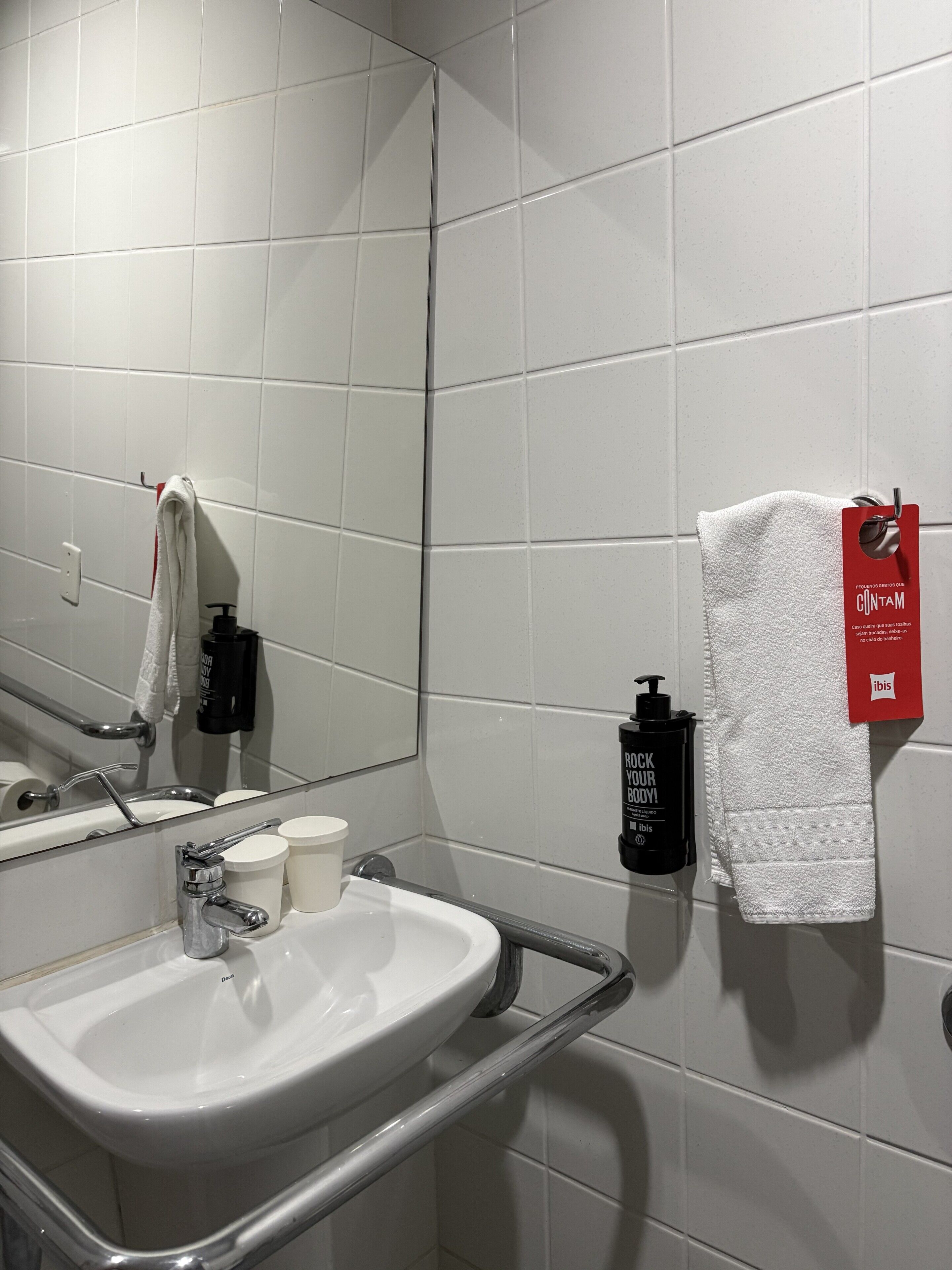 Un baño con lavamanos blanco, espejo, toallero y artículos de aseo.