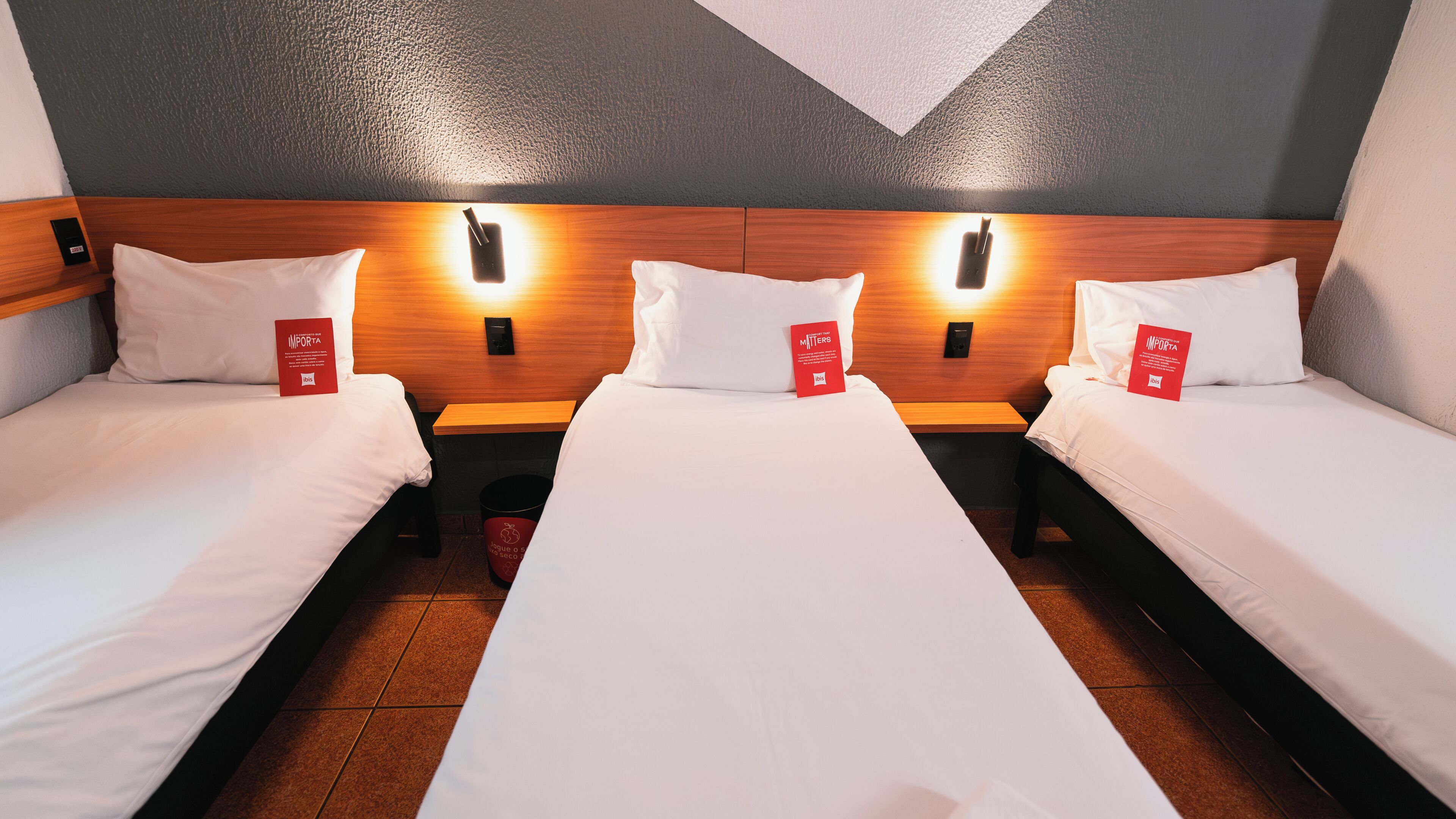 Ein Hotelzimmer mit drei Einzelbetten, jedes mit einem Kopfkissen und einem roten Etikett.