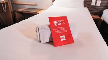 A neatly made bed with a red tag on the pillows, a wooden headboard, a bedside table, and a wall-mounted lamp.