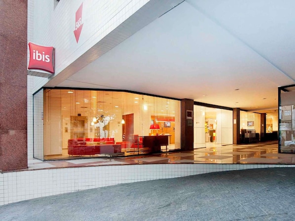 Ein Hotel Eingang mit einer großen Glasfassade, einem roten Logo und einem gefliesten Boden.