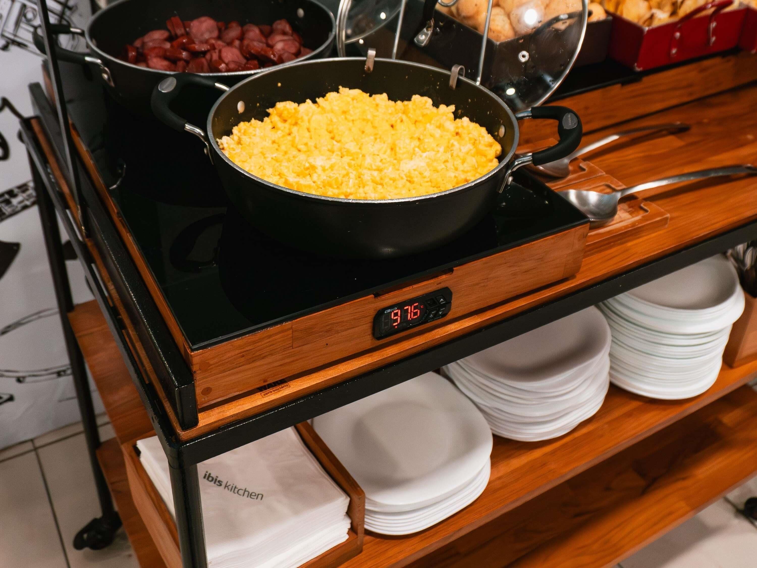 Una encimera de cocina con una sartén, una olla con huevos revueltos y un reloj digital que muestra las 9:76.