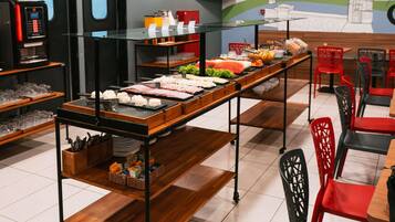 A buffet setup with various food items, a coffee machine, and red chairs.