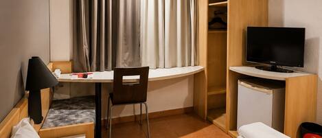 A hotel room with a bed, desk, chair, television, wardrobe, and curtains.