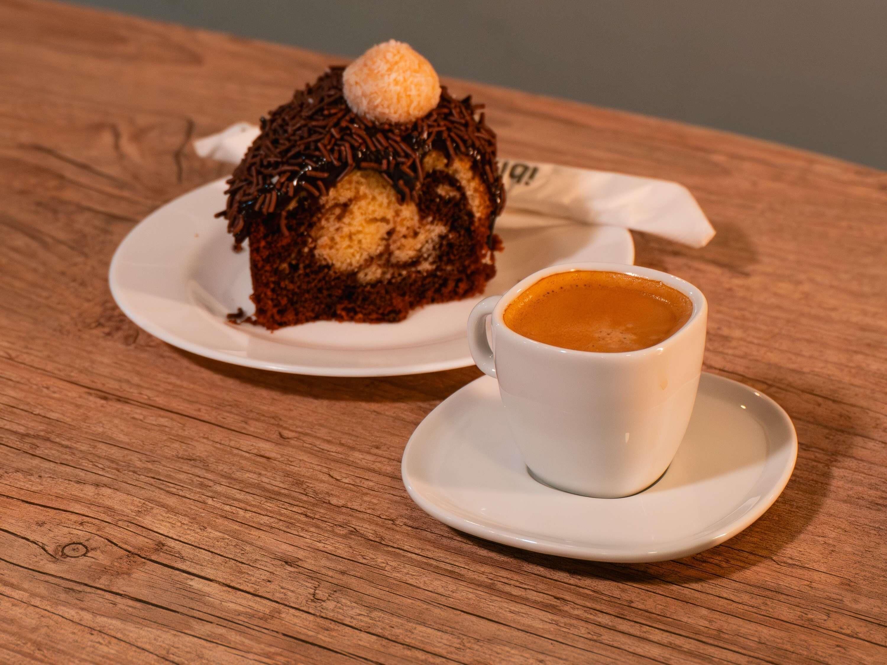 A slice of cake with a dollop of cream on top, accompanied by a cup of coffee on a wooden table.