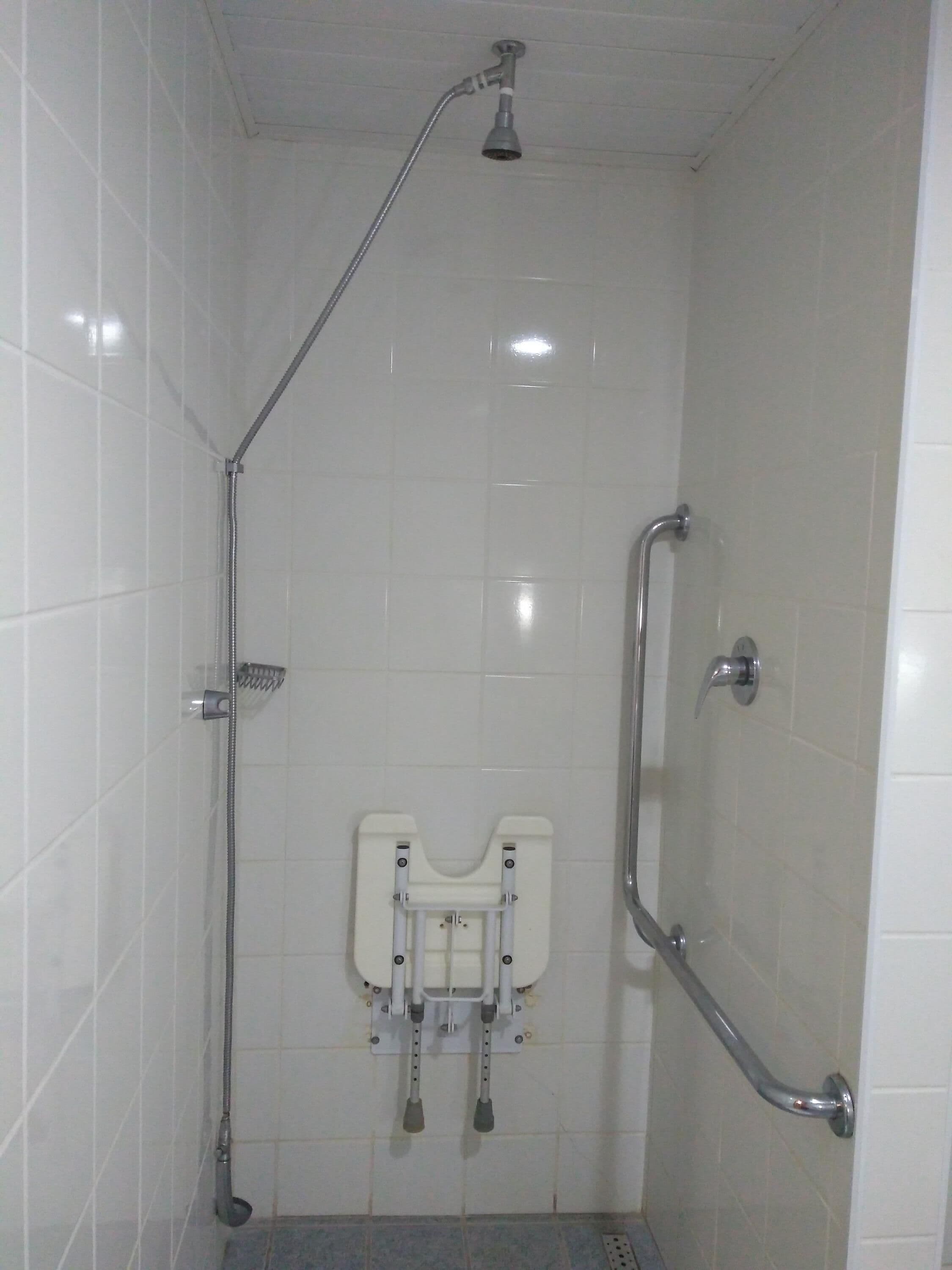 Ducha con barra de apoyo, cabezal de ducha de mano y asiento fijado a la pared.